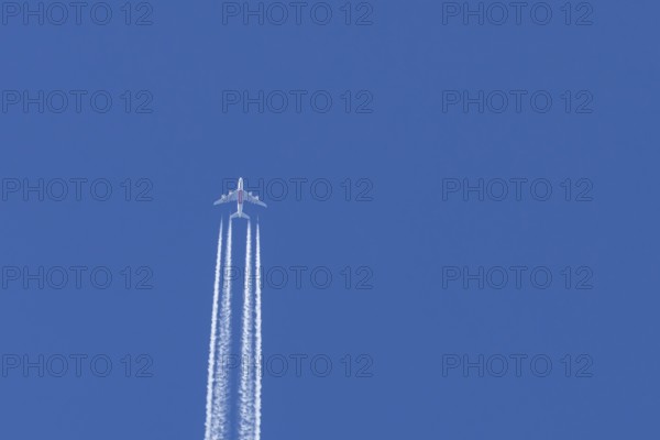 Airbus A380 jet passenger aircraft of Emirates airlines flying in a blue sky with contrails or