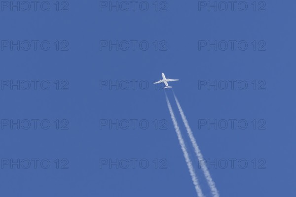 Jet passenger aircraft flying in a blue sky with contrails or vapour trails behind, England, United