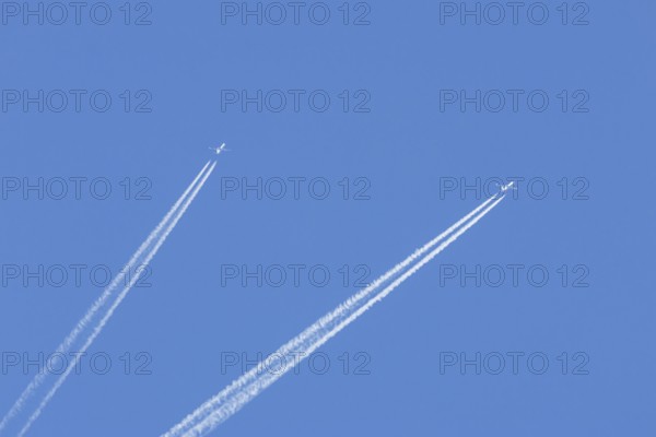 Two jet passenger aircraft flying in a blue sky with contrails or vapour trails behind, England,