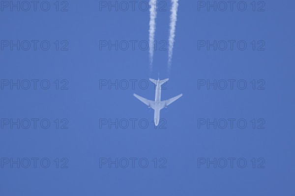 Jet passenger aircraft flying in a blue sky with contrails or vapour trails behind, England, United