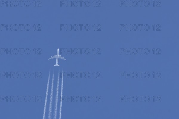 Jet passenger airliner aircraft flying in a blue sky with contrails or vapour trails behind,