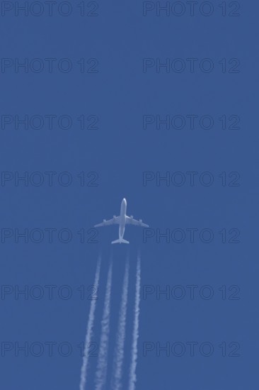 Jet commercial passenger aircraft flying in a blue sky with contrails or vapour trails behind,