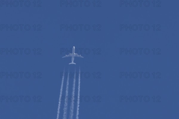 Jet commercial passenger aircraft flying in a blue sky with contrails or vapour trails behind,