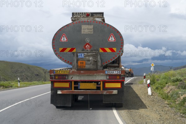 A truck drives on a winding road through a mountainous landscape under cloudy sky, truck with