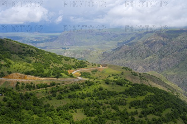 Wide green landscape with hills and a winding road under cloudy sky, landscape near Ltsen, Syunik