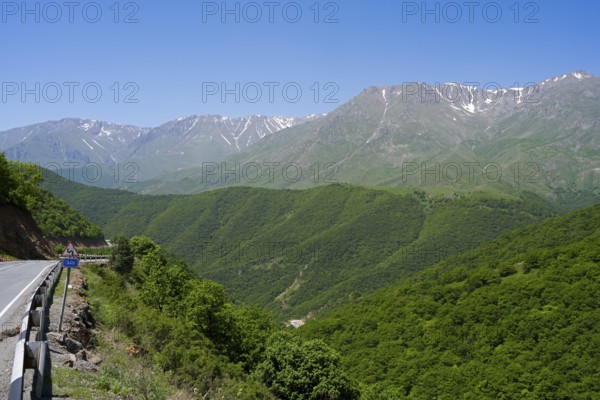 A winding mountain road snakes through green hills with mountains in the background, landscape on