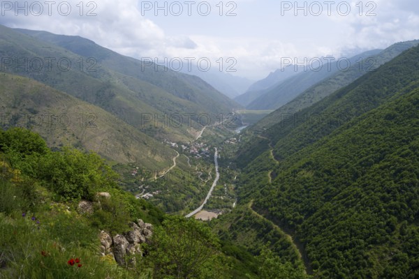 Extensive mountain landscape with a river surrounded by lush vegetation and clouds in the sky, view