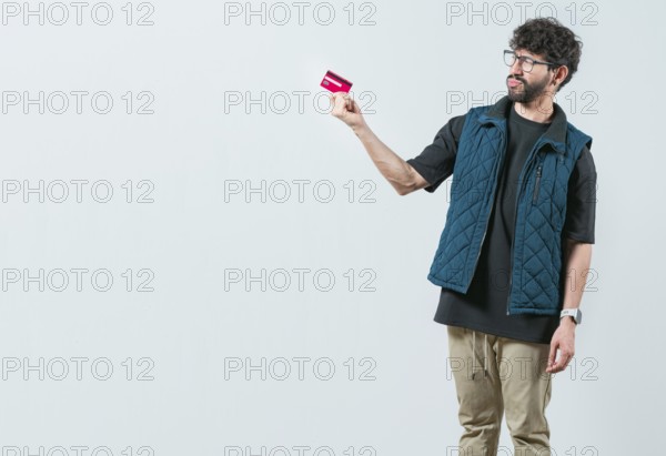 Confused modern guy holding a credit card isolated. Unsure and confused young man holding and