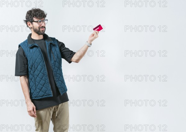 Unsure and confused young man holding and looking at a credit card. Confused modern guy holding a