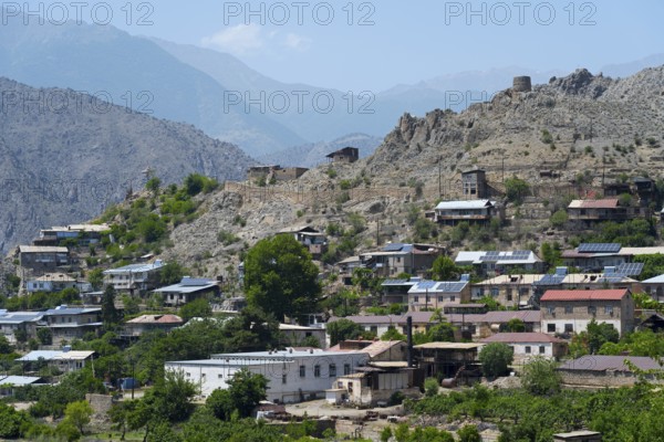 Hilly landscape with a village using solar panels, surrounded by rocky mountains in sunny weather,