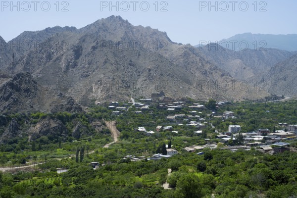 Mountain village with lush vegetation, surrounded by imposing mountains and clear blue sky, Meghri,