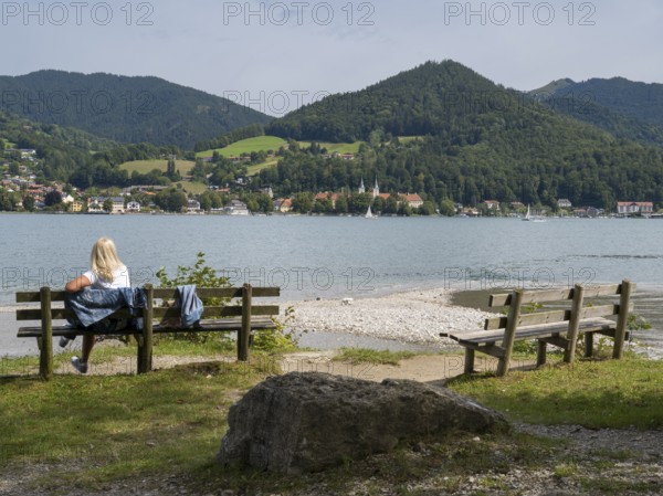 View of Tegernsee with castle, woman sitting on a bench, Bad Wiessee, Upper Bavaria, Bavaria,