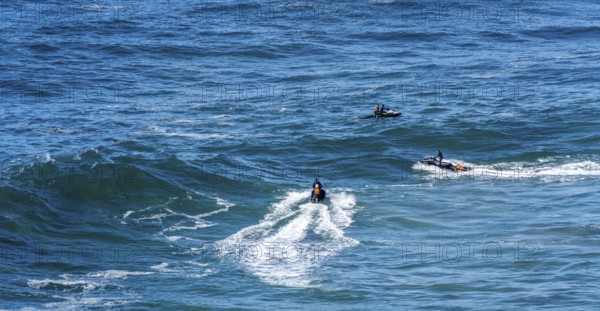 Surfers with their jet ski pilots in the Atlantic waves below Farol de Nazaré, Forte São Miguel,