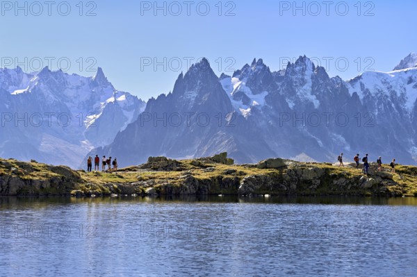 A group of hikers at Lac de Chésserys, behind the snow-covered Mont Blanc massif,