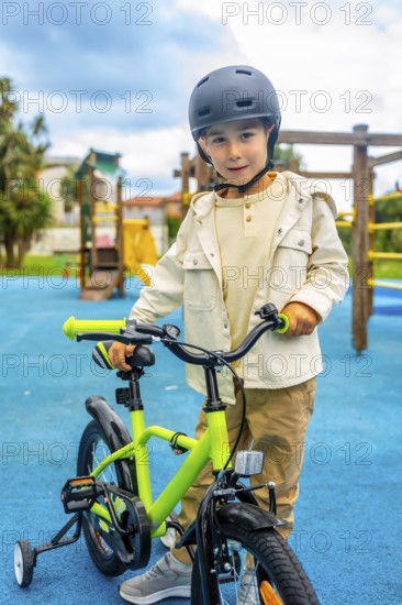 Young boy wearing a helmet standing and holding the handlebars of his bicycle with training wheels