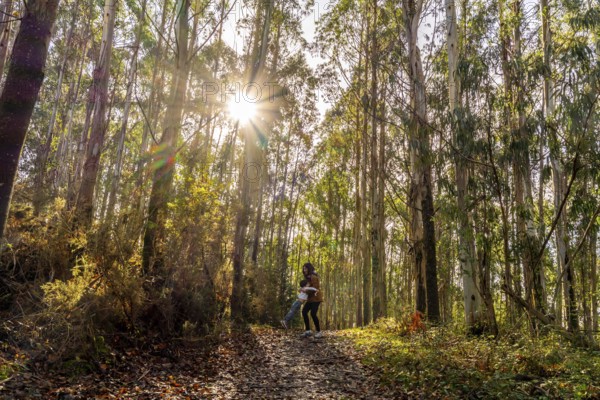 Happy mother spinning her child on a forest path, creating a joyful moment under the sunburst in