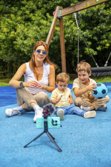 Content creator filming a video with two children at a playground, using a smartphone, microphone,