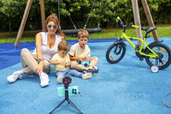 Influencer mother recording a video with her two sons at playground using a smartphone and