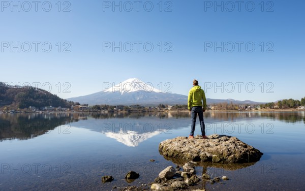 Young man standing on a rock in water, volcano Mt. Fuji is reflected in Lake Kawaguchi, Yamanashi
