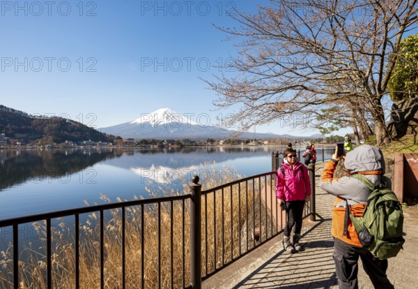 Tourists take pictures on the waterfront, Volcano Mt. Fuji is reflected in Lake Kawaguchi,