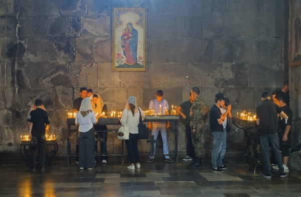 People gather in a church praying, surrounded by burning candles and murals, in a thoughtful mood,