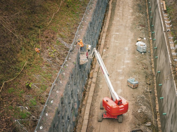 Construction workers on a lift attach a net to a steep slope, construction of the Hermann Hesse