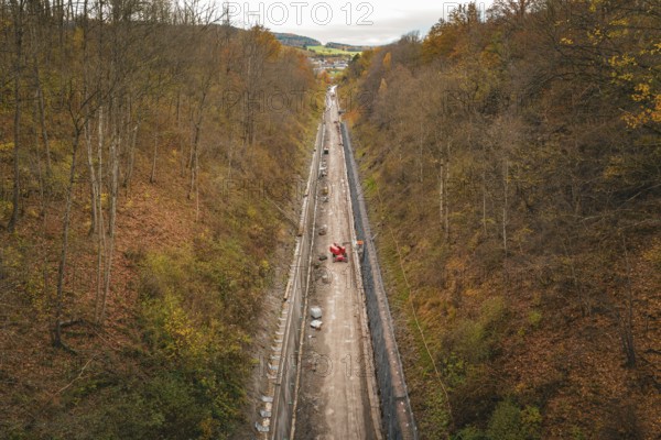 Aerial view of a construction site in an autumnal forest, with a long area of soil between steep