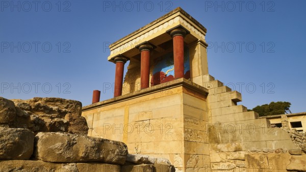 Ancient ruins with typical red Minoan columns and wall painting, under blue sky on the island of