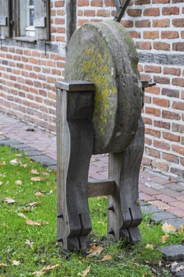 Old whetstone on wooden stand surrounded by grass and brick buildings, Münsterland, North
