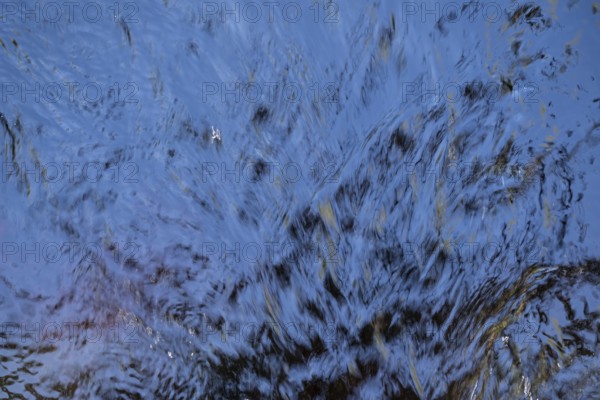 Shimmering blue water surface of a stream, current, light reflections, abstraction, long exposure,
