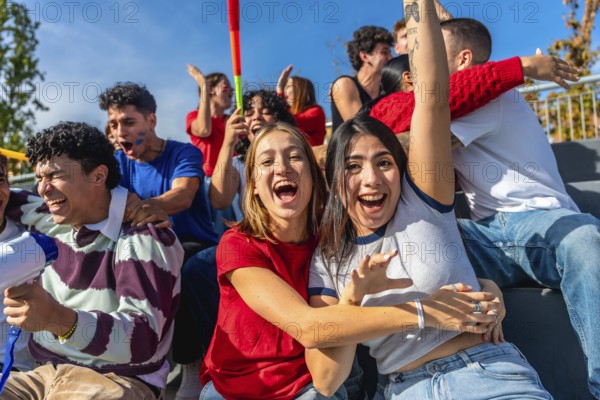 Cheerful young friends sitting in stadium stands, actively cheering and celebrating, enjoying a