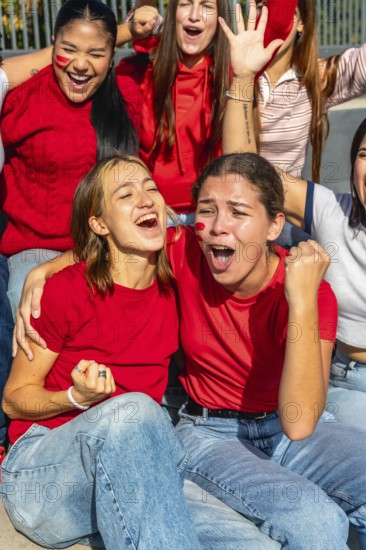 Group of enthusiastic women wearing red shirts and face paint, celebrating with open mouths and