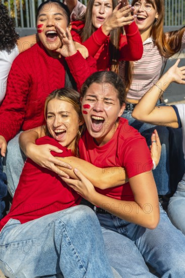 Group of excited young women wearing red, cheering loudly with face paint on their cheeks,