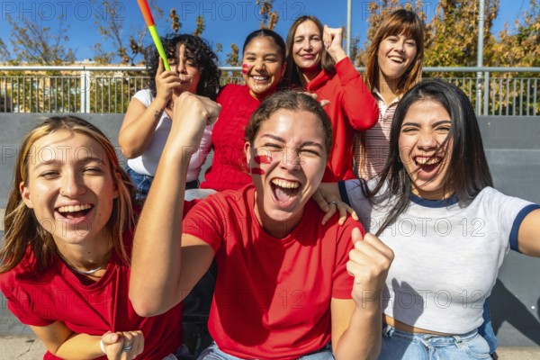 Diverse group of young women cheering loudly in a stadium, faces painted and fists raised,