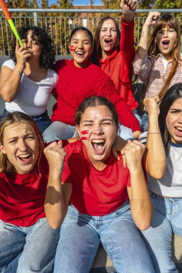 Group of excited young women with face paint and red clothing cheering passionately during a