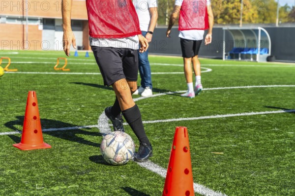 Football player practicing drills with ball and cones on artificial green turf, focused on