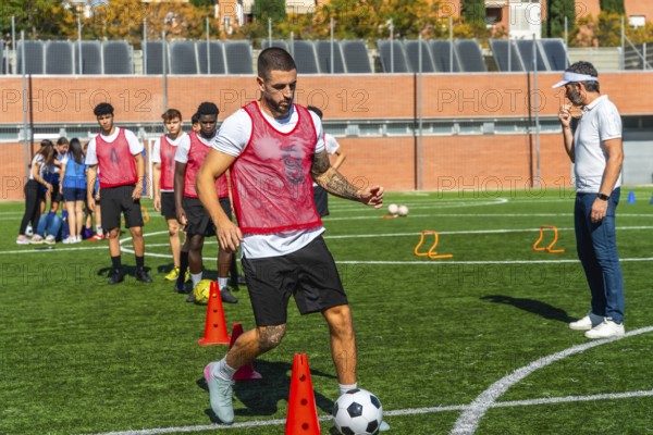 Soccer player in a red bib training on a green artificial turf field, dribbling a football around