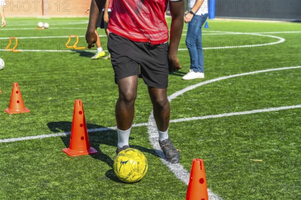 Young player actively training and practicing soccer drills, dribbling the ball around orange cones
