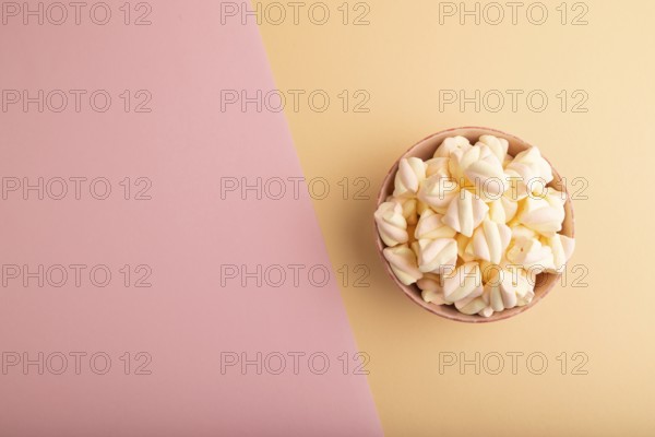 Orange and pink marshmallow in ceramic bowl on pink and orange pastel paper background, top view,