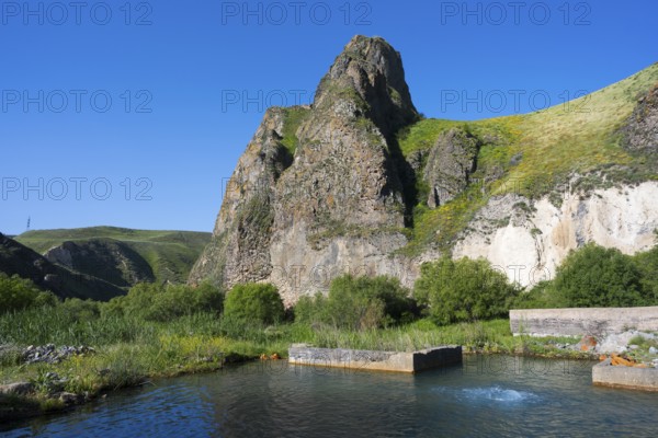 Clear water with spring flows through a lush landscape dominated by huge, rocky mountains, hot