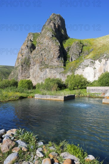 Clear water flows through a green landscape, framed by majestic, sunlit rocks, hot spring, Vorotan,