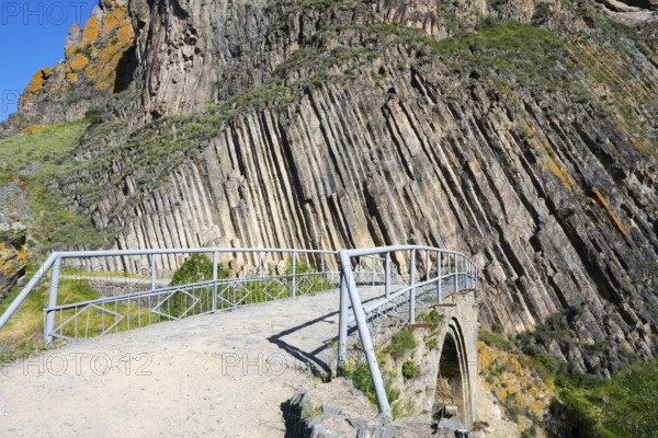 A narrow path with railing leads over a stone bridge, surrounded by unique vertical rock