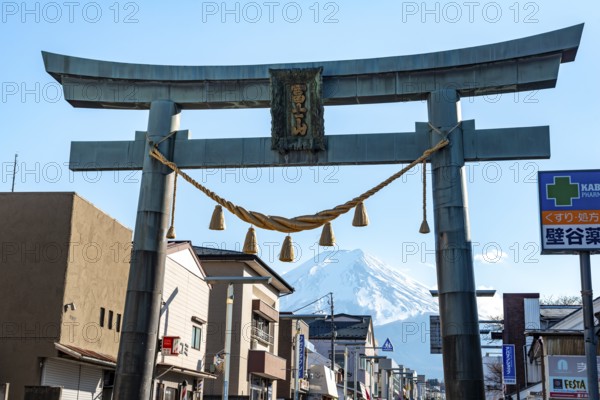 Large torii gate on above a street, street scene, in the back volcano Mt. Fuji, Fujiyoshida,