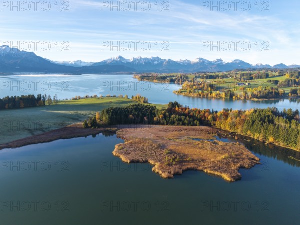Clear lake, surrounded by autumn trees, with alpine peaks on the horizon under clear sky,
