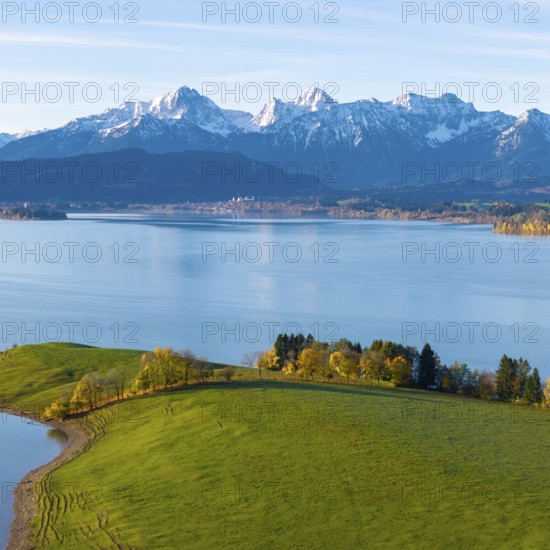 Green hills and trees on the shores of a quiet lake against the backdrop of majestic alpine