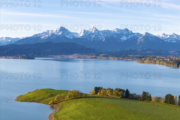 View over quiet lake and rolling hills to the chain of snow-capped alpine mountains in the