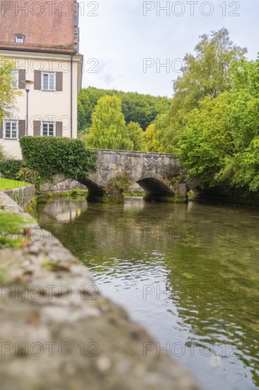 An old stone bridge over a quiet river flanked by buildings and trees, ZFP Zwiefalten, Reutlingen