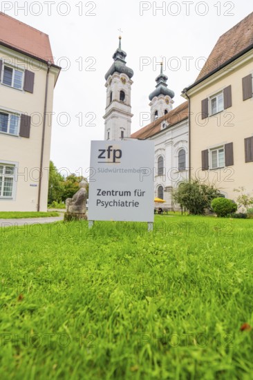 Sign for the Center for Psychiatry with two church towers in the background on a green field, ZFP