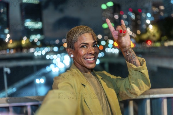 Happy woman with short blond hair and a tattoo making a rock and roll hand gesture, smiling at the