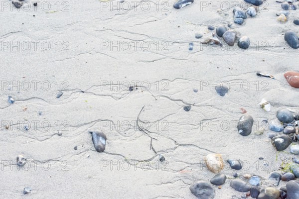 Pattern in sand with scattered stones on a quiet sandy beach, drainage channels, runoff water,